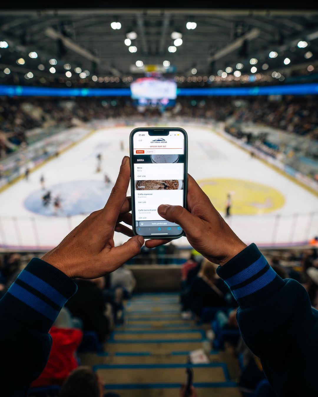 A spectator orders from their phone in the stands, with the ice rink below.