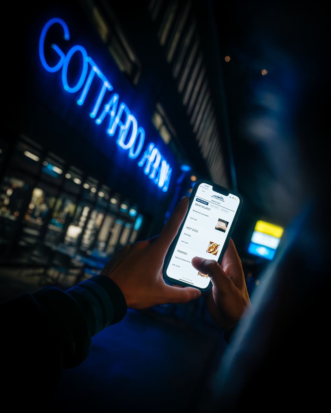 The Gottardo Arena sign lit at night, a guest ordering from a phone below it.
