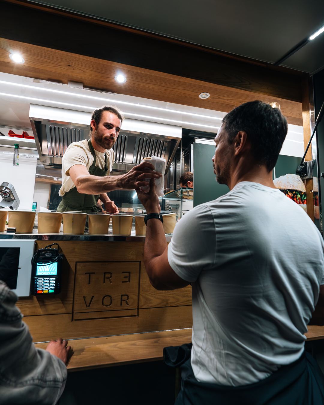 Le personnel prépare une commande derrière le comptoir pendant qu'un client paie au terminal.